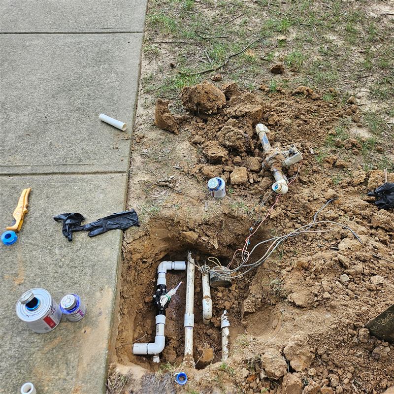 Exposed irrigation valve and PVC piping during repair beside a sidewalk